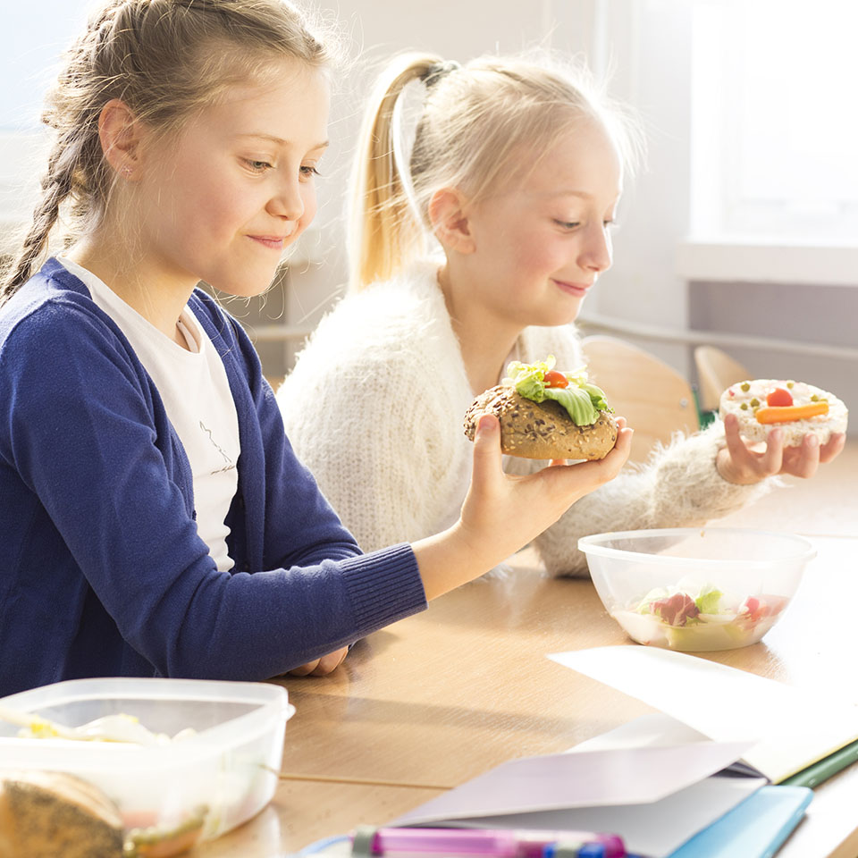 Two young pretty girls eating together healthy sandwiches during lunch break at school